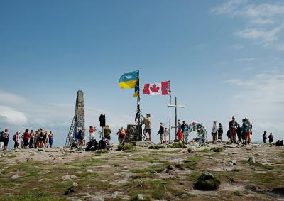 Туристи поряд з українським та канадським прапорами на вершині Говерли